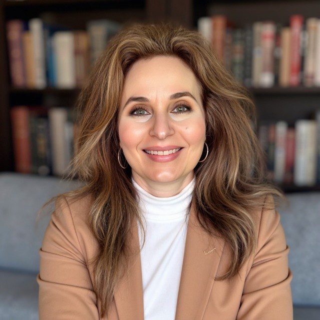 Smiling woman in a brown blazer and white turtleneck in a cozy library setting.